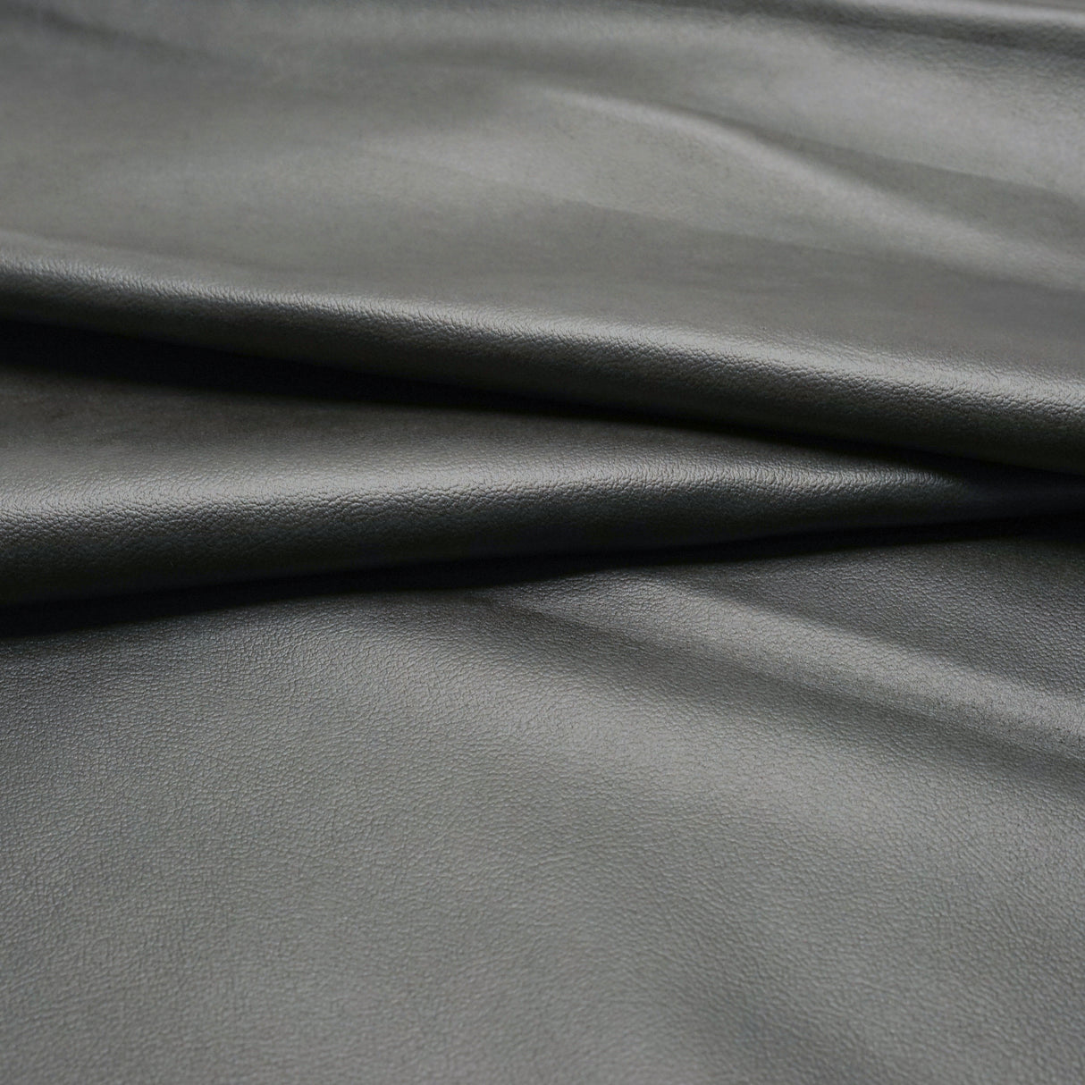 A close-up of dark gray pebbled leather
with soft folds and a smooth texture.