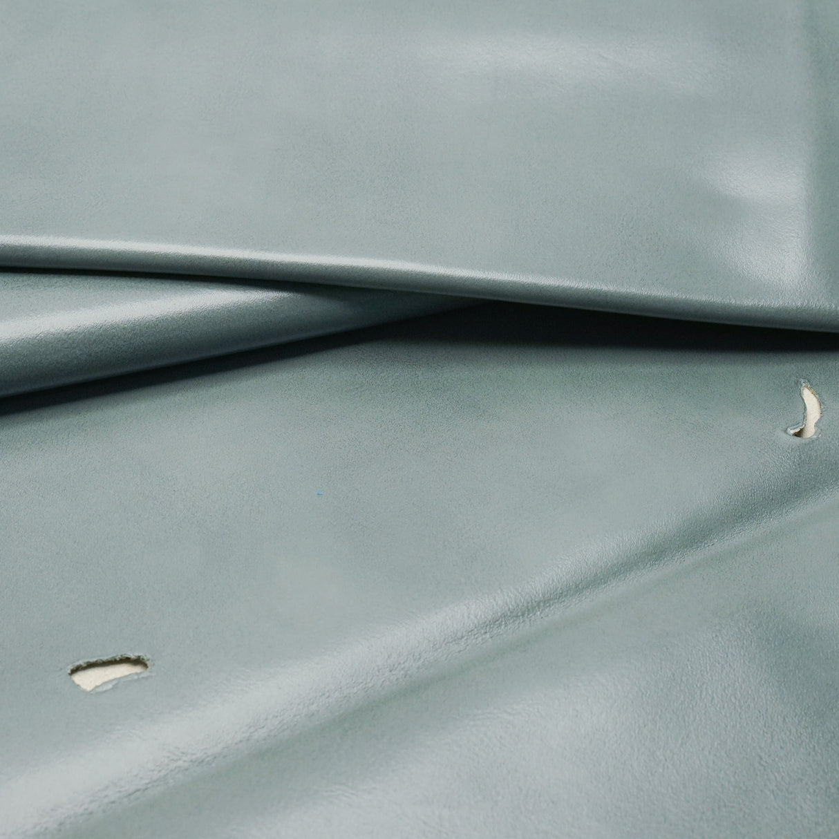 A close-up of a smooth, slightly glossy fabric or material in a muted blue-gray color, folded to show texture and drape.