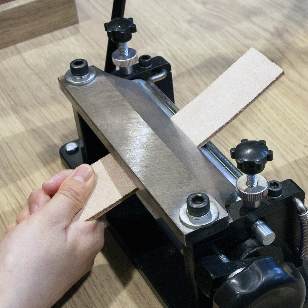 Black and silver splitting machine with leather being pulled through with a hand.
