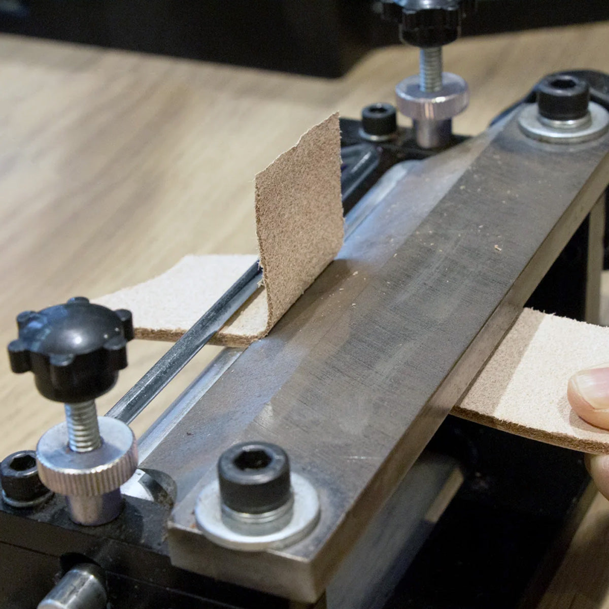 Black and silver splitting machine with leather being pulled through with a hand.