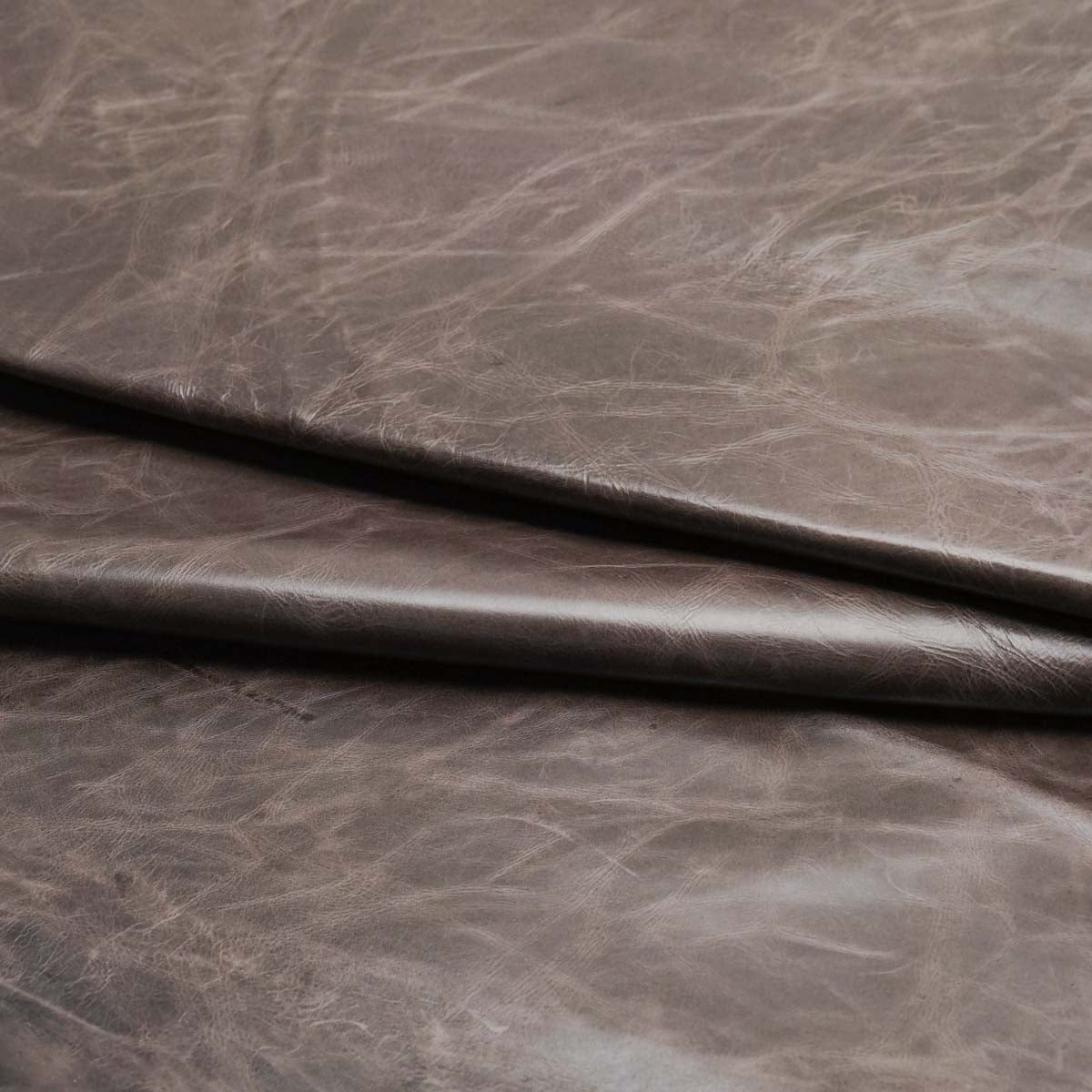 A close-up of dark brown textured leather fabric with visible grain and a folded crease running diagonally across the frame.