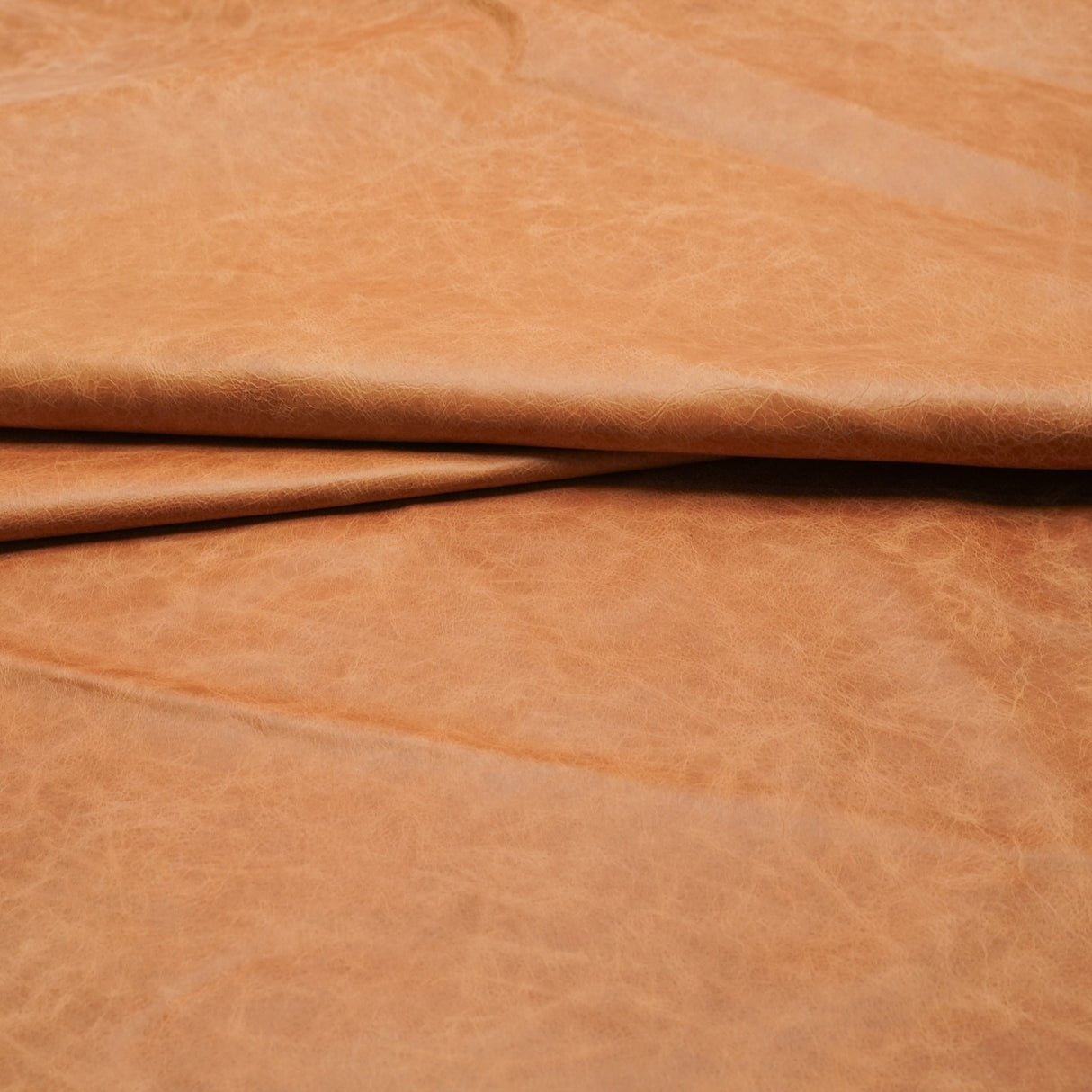 A close-up of draped tan leather with a soft, slightly textured surface.