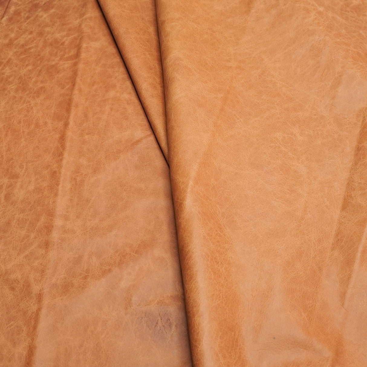 A close-up of draped tan leather with a soft, textured surface and natural folds.