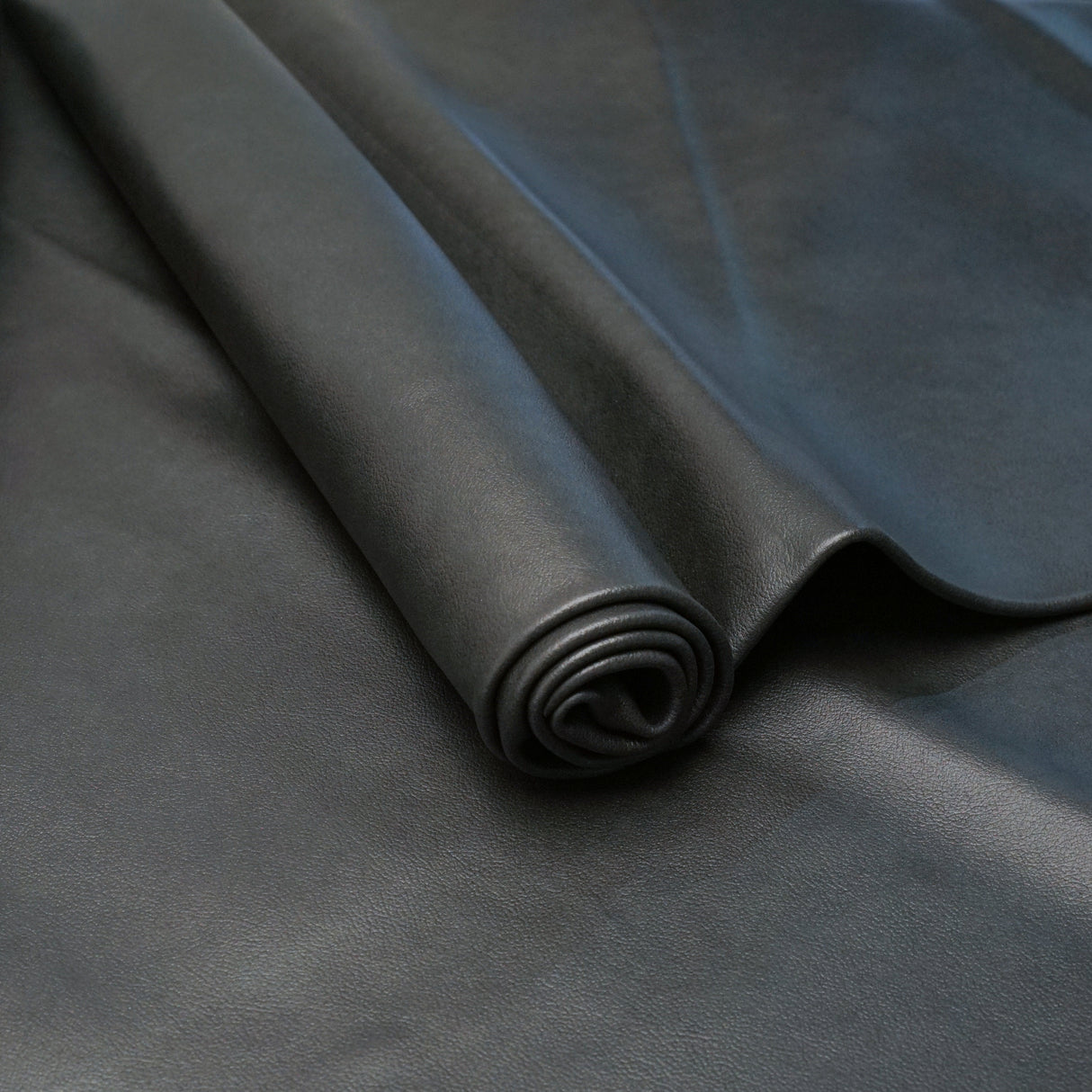A close-up of a dark charcoal gray roll of material, likely leather, draped over a matching flat surface.