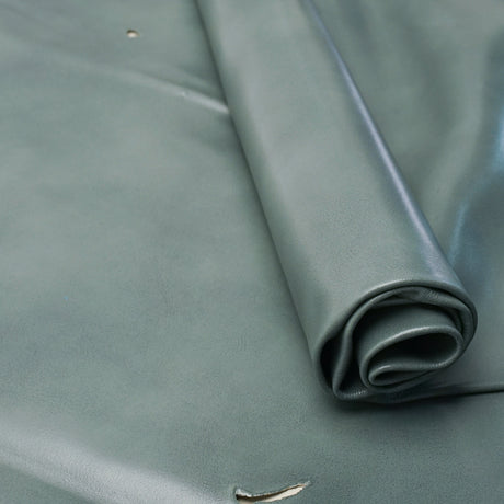 A close-up of a rolled piece of smooth leather in a muted sage green color, laid out on a matching background.