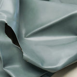 A close-up of draped light blue-gray material with a glossy finish and a torn section revealing a dark interior.