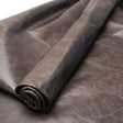 A close-up of rolled dark brown leather fabric with a textured, slightly distressed finish, shown against a matching background.