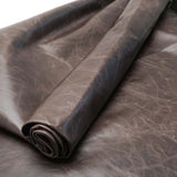 A close-up of rolled dark brown leather fabric with a textured, slightly distressed finish, shown against a matching background.
