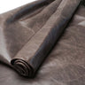 A close-up of rolled dark brown leather fabric with a textured, slightly distressed finish, shown against a matching background.