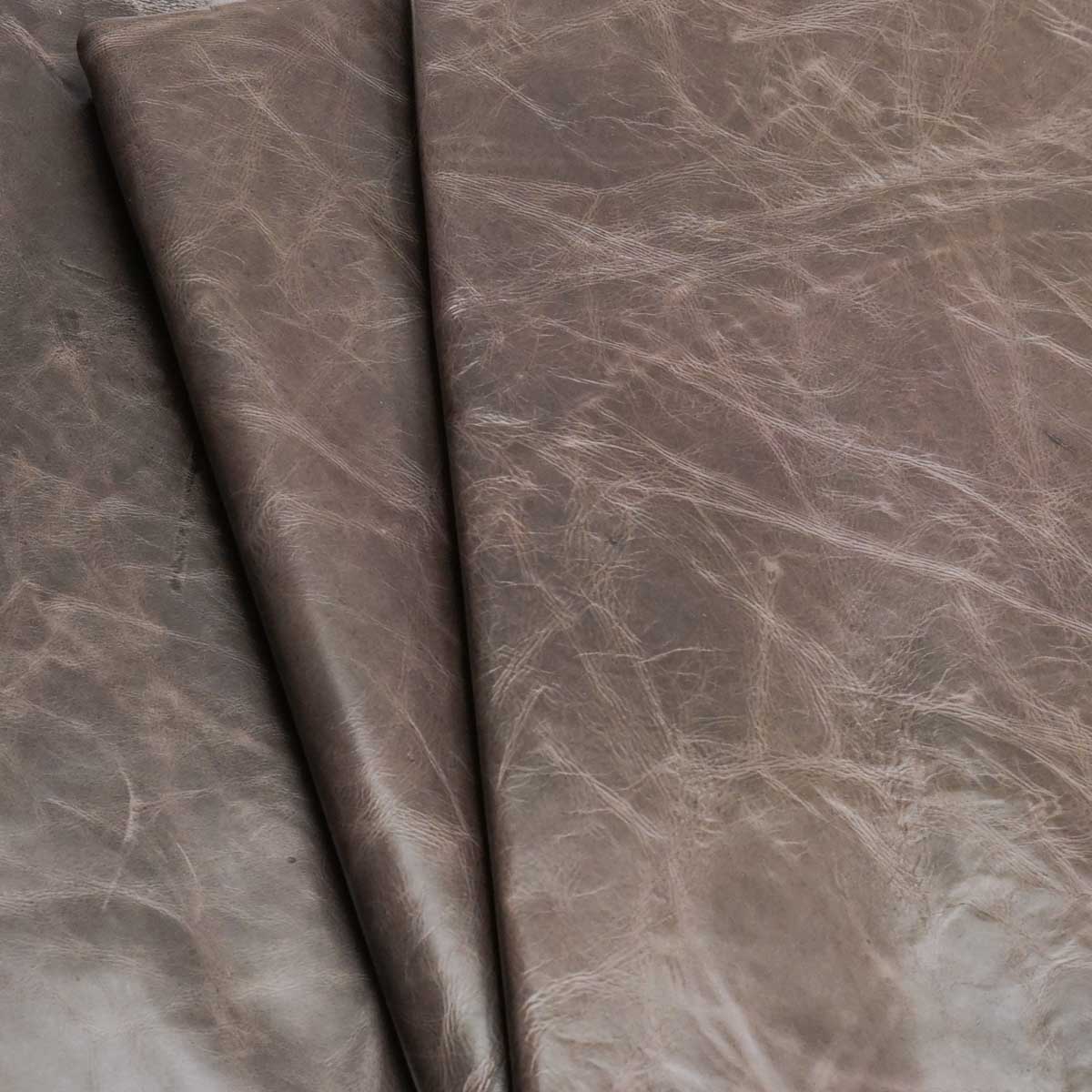 A close-up of draped textured leather fabric in a taupe-brown color with natural creases and a slightly distressed finish.