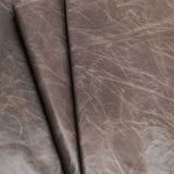 A close-up of draped textured leather fabric in a taupe-brown color with natural creases and a slightly distressed finish.