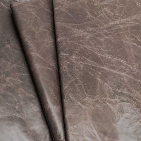 A close-up of draped textured leather fabric in a taupe-brown color with natural creases and a slightly distressed finish.