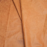 A close-up of draped tan leather with a soft, textured surface and natural folds.