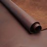 A roll of dark brown leather material placed diagonally across a smooth matching brown surface.