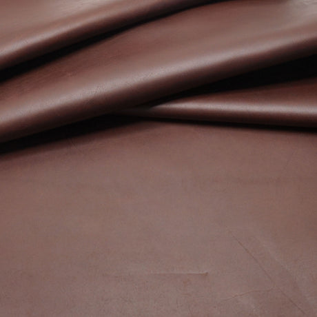A close-up of draped brown leather fabric showing its smooth texture and soft folds.