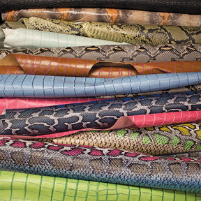 Assorted odd lot embossed leather remnants showing textured alligator, snake, and lizard prints for custom leatherworking and crafts.